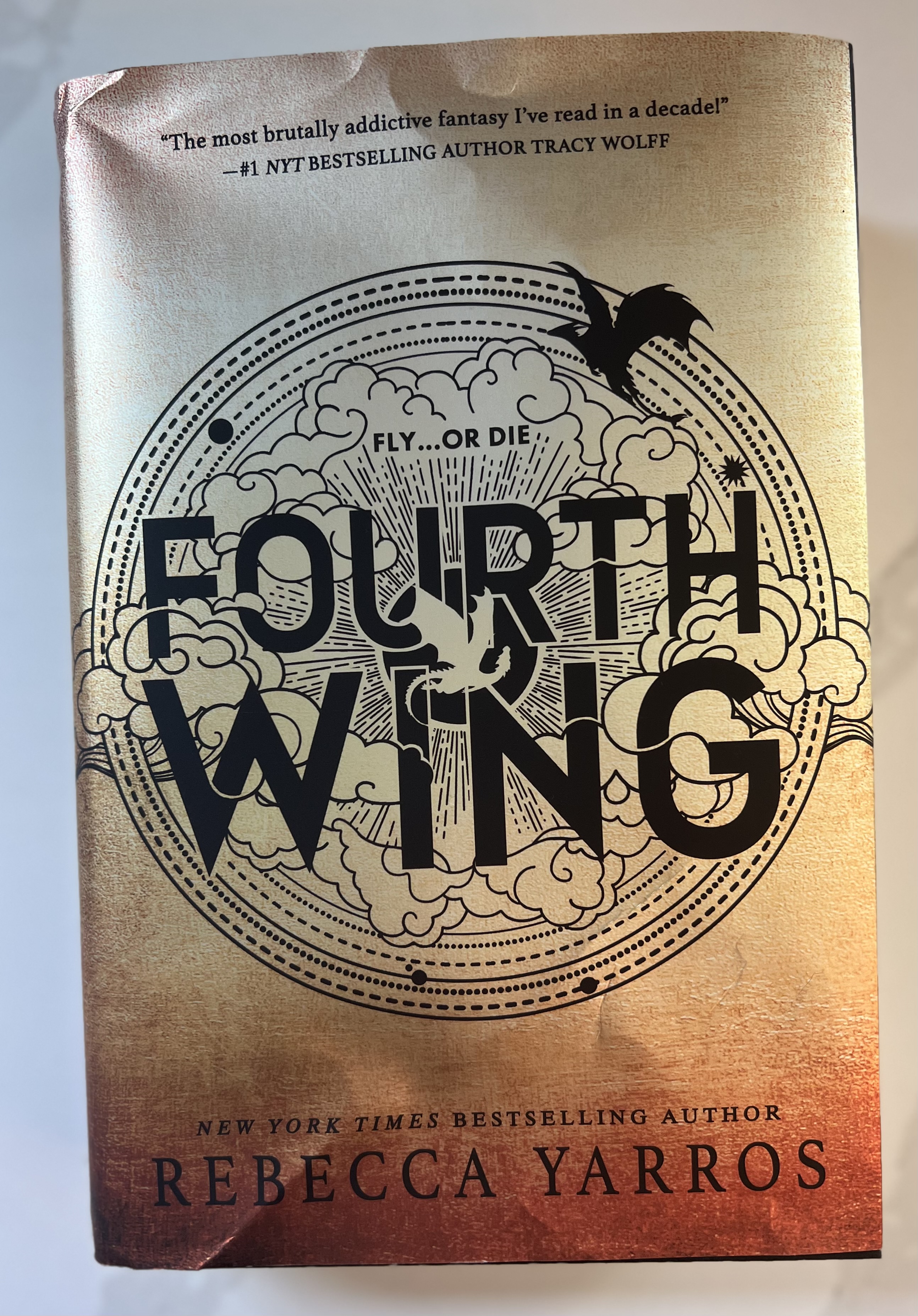 This is a photograph of the book Fourth Wing by Rebecca Yarros; sitting on a white countertop.