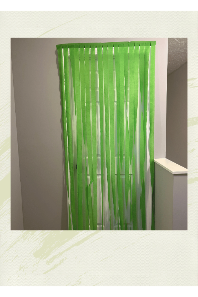 A photograph of a bedroom door with green streamers hanging down from the top to the bottom of the door. To show the birthday tradition for kids of a birthday morning surprise.