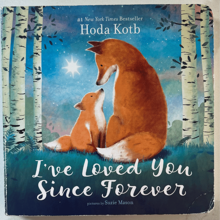 A photograph of the book cover of I've Loved You Since Forever sitting on a white counter top. The book cover has one large orange fox and one orange baby fox looking at each other sitting on blueish green grass in-between birch trees with the night sky in the background with one large star. The words "#1 New York Times Bestseller Hoda Kota" are at the top and the words "I've Loved You Since Forever" centered at the bottom.