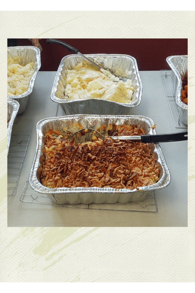 A photograph of large tins with takeout food in them. One with mash potatoes and another with a casserole. Showing the new mom gift idea of providing meals.