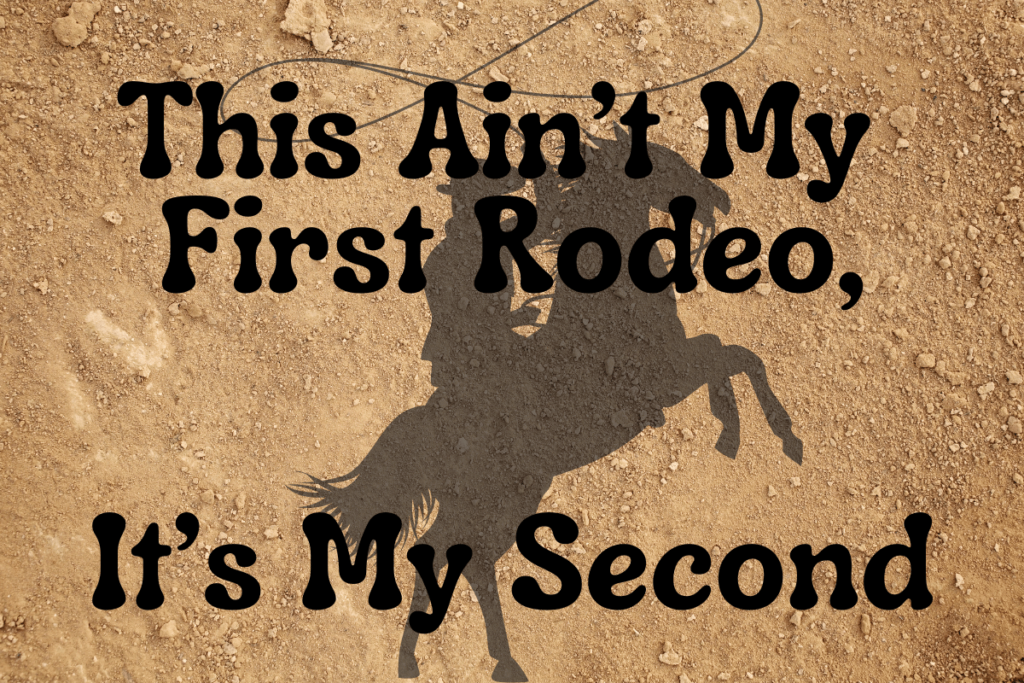 The background of the graphic is a dirt ground. On the dirt ground is a shadow of a cowboy on on a course on its back two feet. The top center has the words "This Ain't My First Rodeo," and at the bottom as the words "It's My Second".