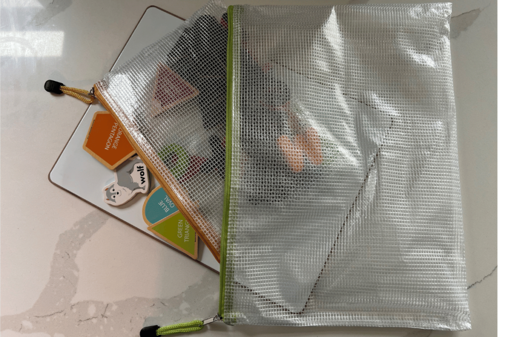 Picture of a white rectangle magnet board with a small mesh zipper bag full of small magnets designed for kids spilling out of the small bag on top of the magnet board. All in a larger mesh zipper bag.