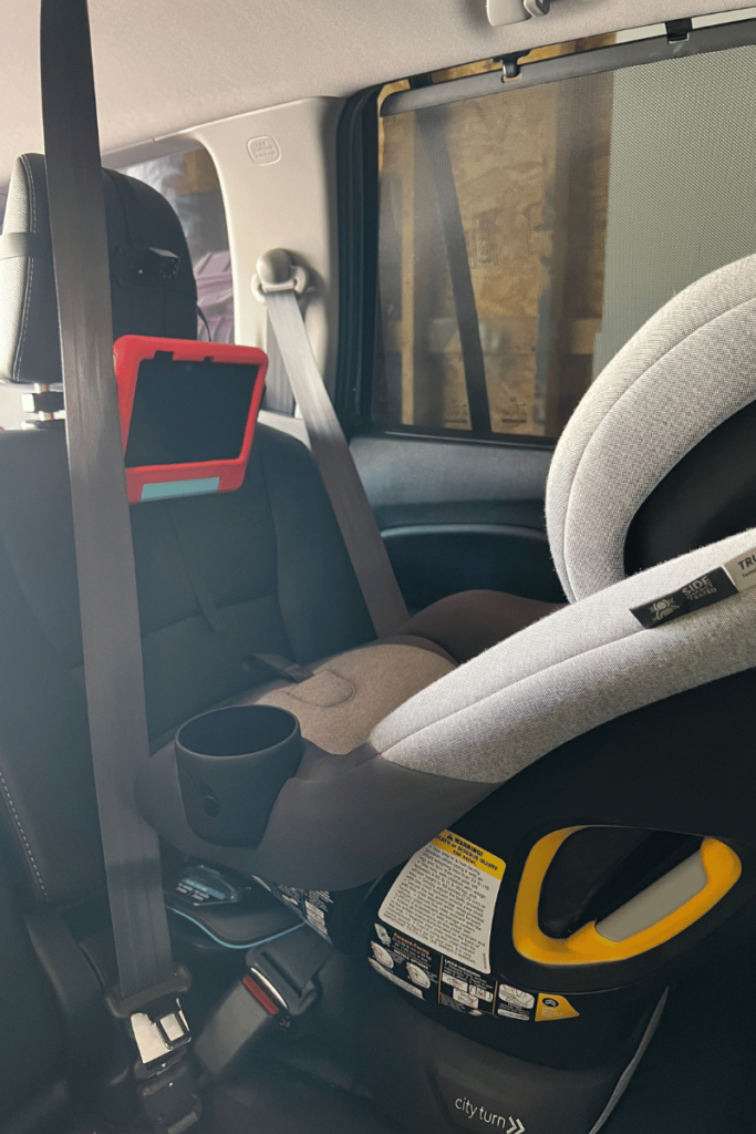 Picture of the back seat of our car taken from the side with a car seat installed backwards facing. A tablet in a read protective case attached to seat his car seat is installed in.